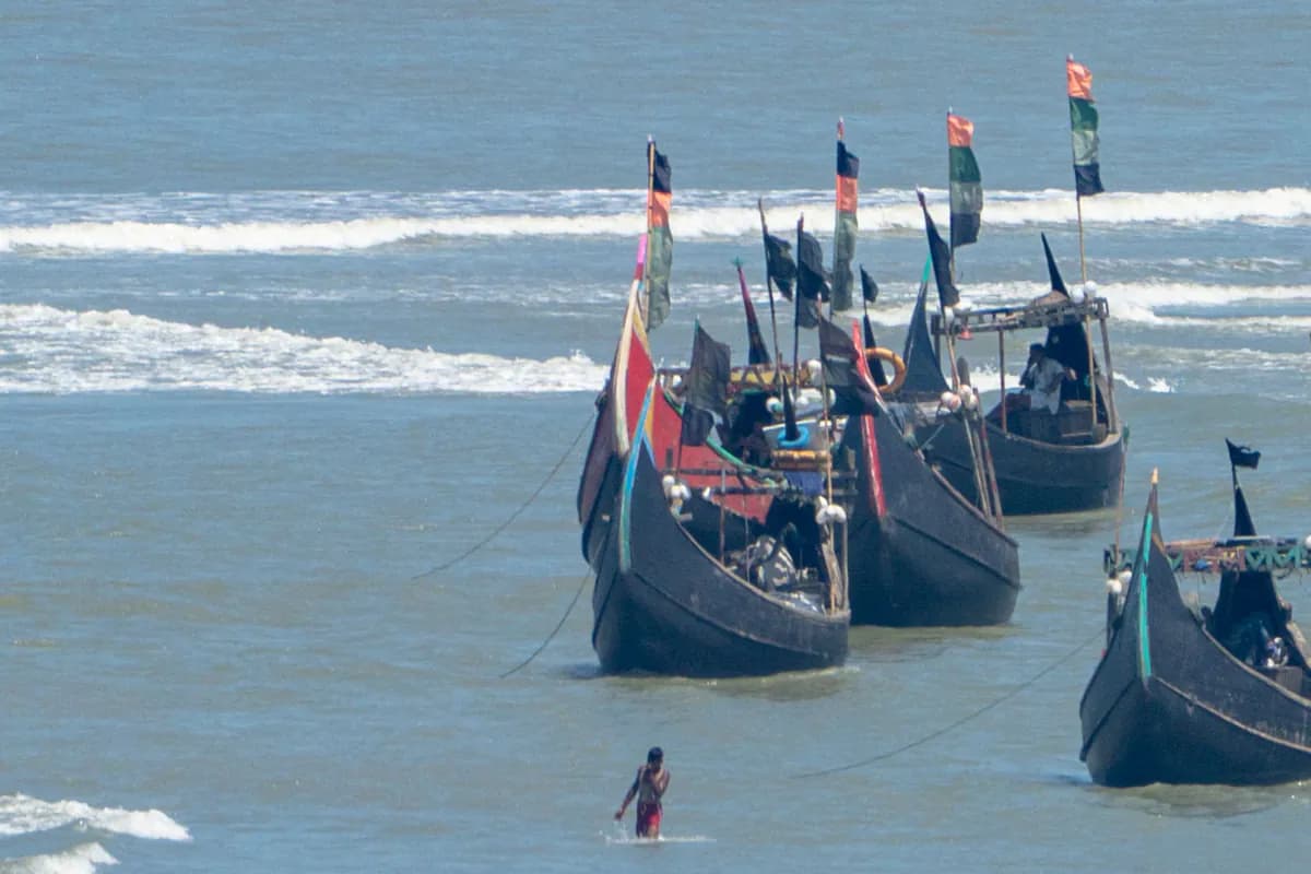 Wooden fishing boats with tall flags anchored in shallow water near the shore, with surf behind
