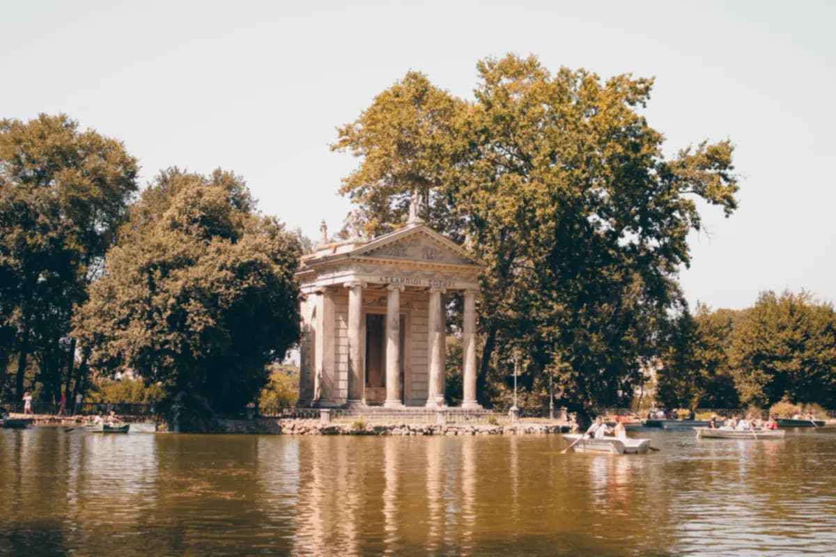 The Temple of Aesculapius on its island in the lake of Villa Borghese, among tall trees, with rowing boats on the water