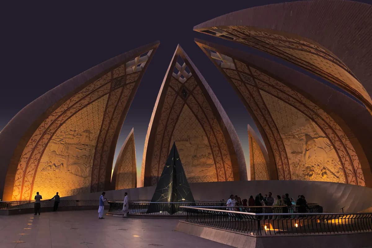 The petal shaped walls of the Pakistan Monument lit up at dusk, with visitors on the platform below