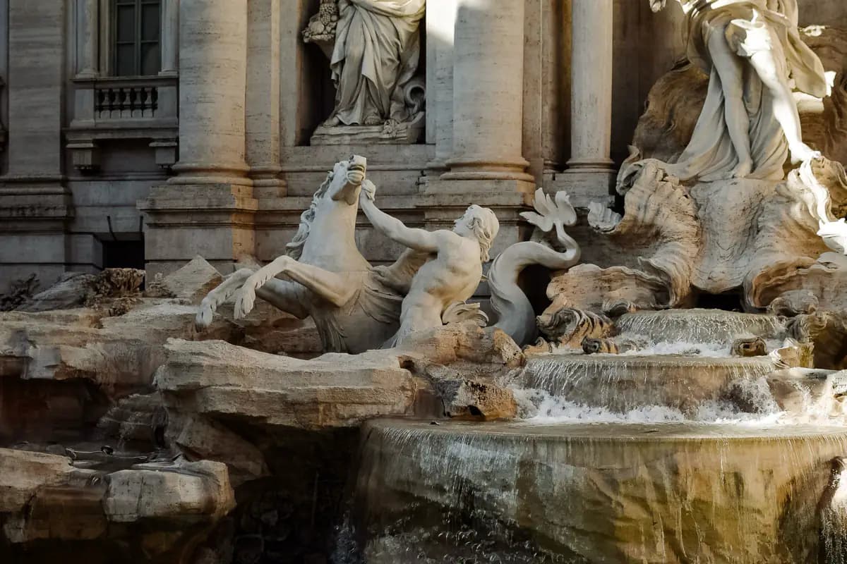 Marble sculptures of a rearing sea horse and a triton above cascading water at the Trevi Fountain in Rome