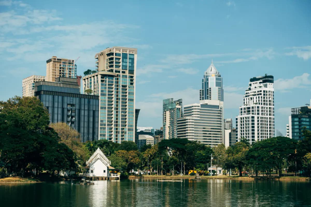 The lake in Lumphini Park with a small white pavilion and trees, and tall city buildings behind