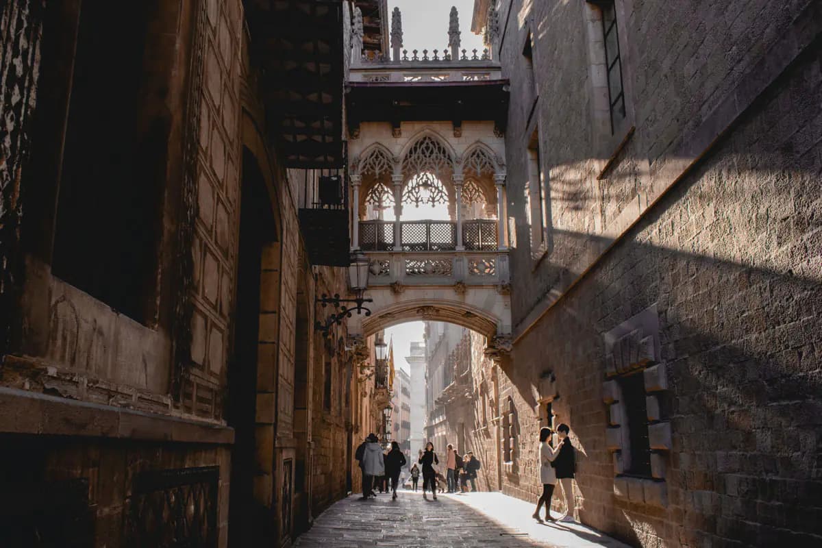 The carved stone Pont del Bisbe crossing a narrow street in the Gothic Quarter of Barcelona, with people walking below