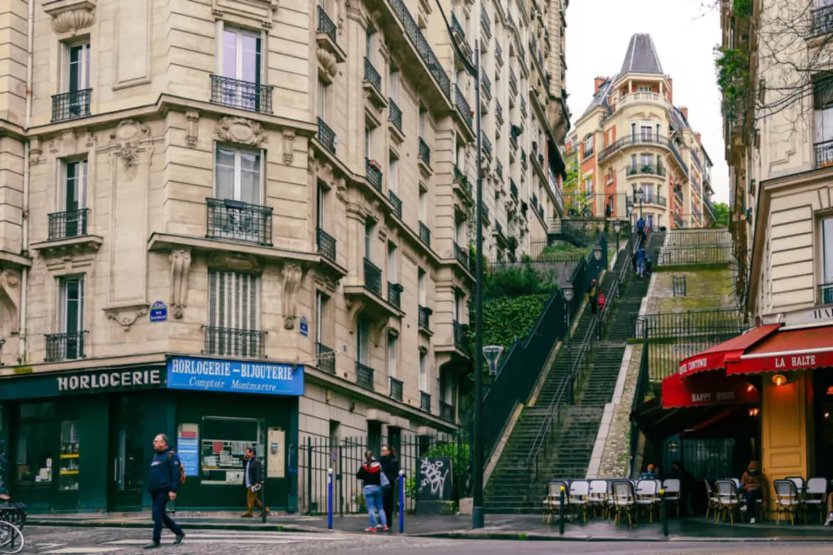 A street corner in Montmartre with stone apartment buildings, a long flight of steps and café tables under red awnings